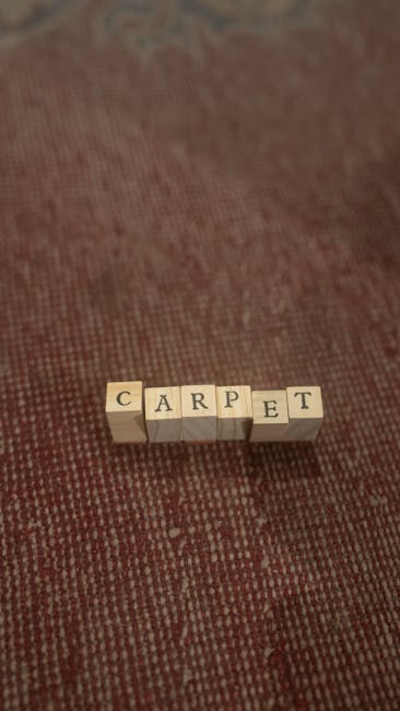 Close-up of a red patterned carpet in a residential or commercial space, featuring small wooden blocks spelling out 'CARPET' placed on the surface. The carpet appears clean and well-maintained with a consistent weave and color. The setting is illuminated by natural or artificial light, highlighting the texture of the fibers. The image illustrates the importance of surface cleaning and maintenance, associated with professional cleaning services offered by Mayfair Carpet Cleaning, focused on deep cleaning and sanitisation of carpets to ensure hygiene and freshness.